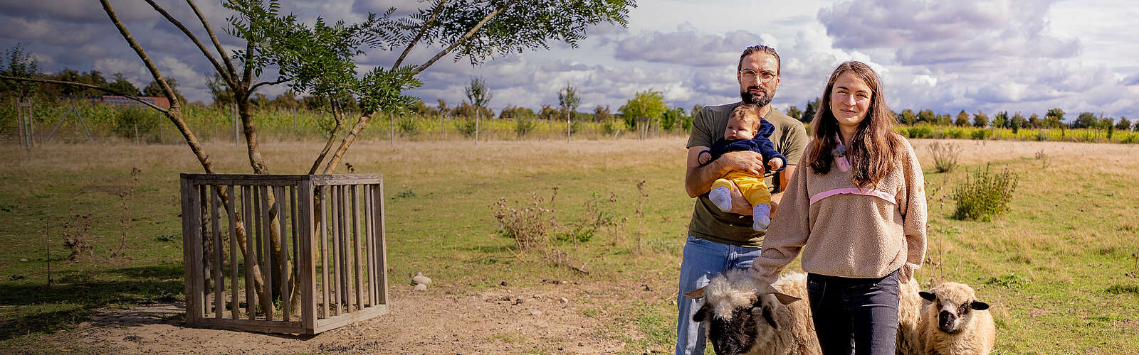 Headerbild, Familie steht auf einer Wiese mit Schafen